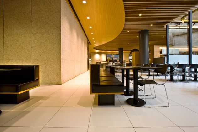 Hall de entrada moderno do hotel com teto curvo de madeira, assentos pretos e janelas amplas.