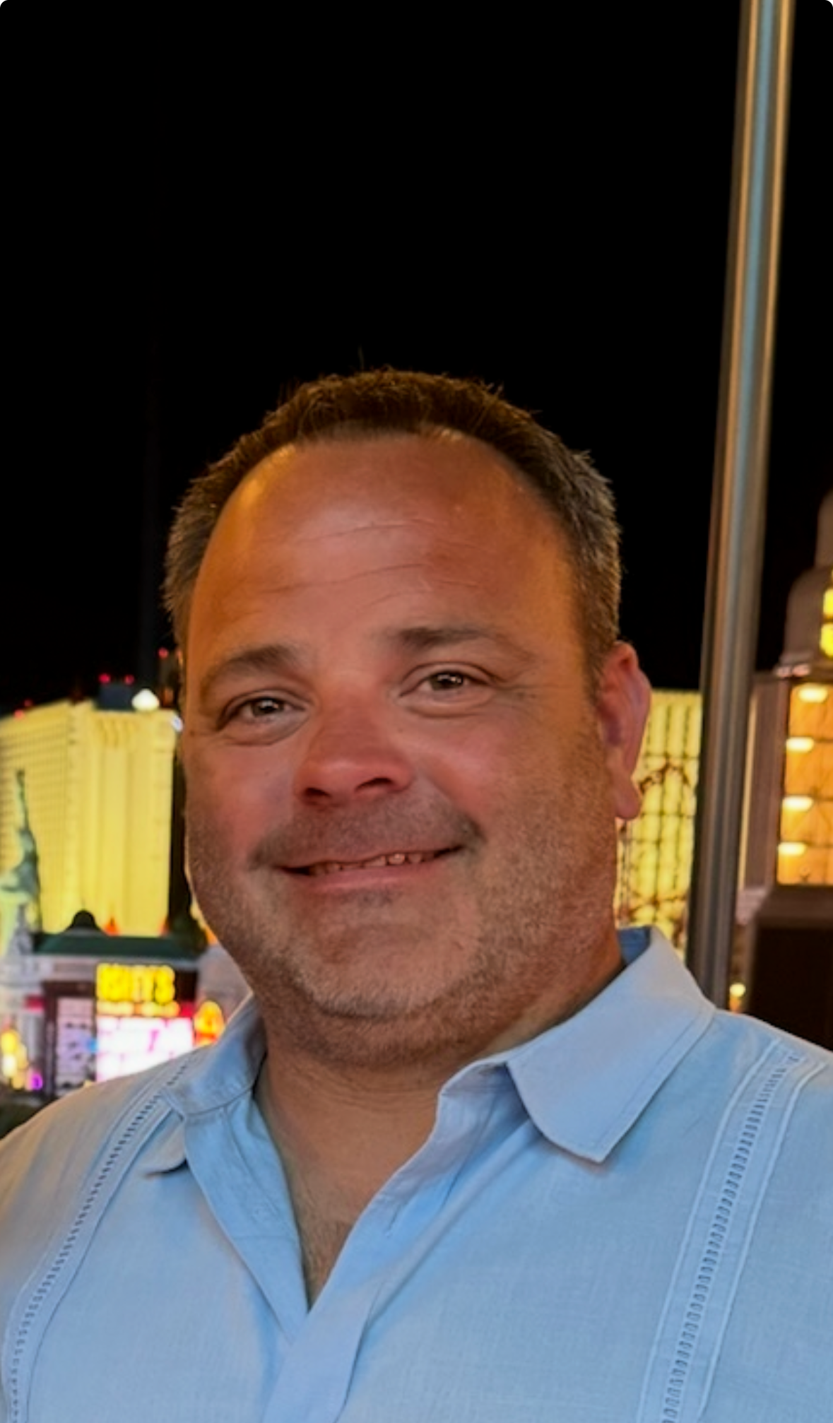 Man in green polo stands on a football field, arms crossed, stadium in background.