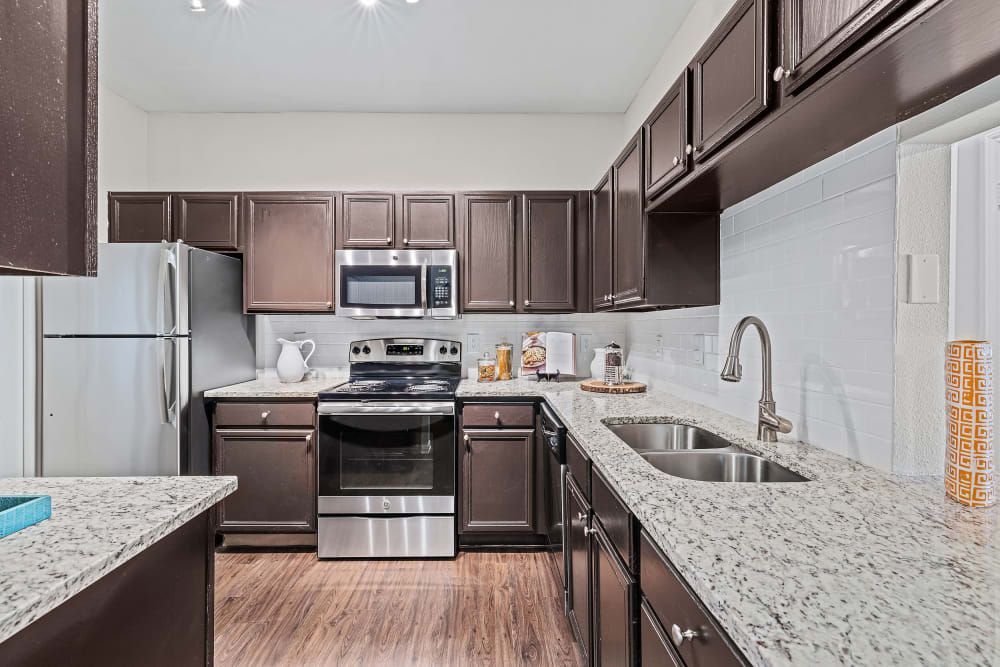 a kitchen with stainless steel appliances, granite counter tops, and brown cabinets at Marquis at Ladera Vista in Austin, TX.