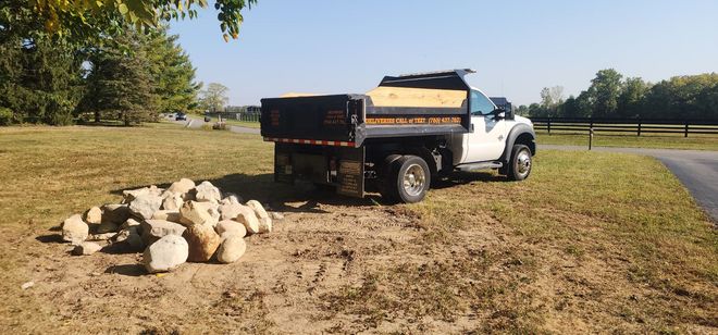 A red truck is towing a trailer full of logs in a grassy field.