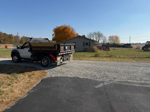 A white dump truck sits on a gravel driveway in a rural setting on a clear, sunny day.