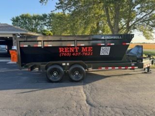 A black Iron Bull dump trailer sits on a paved driveway with 