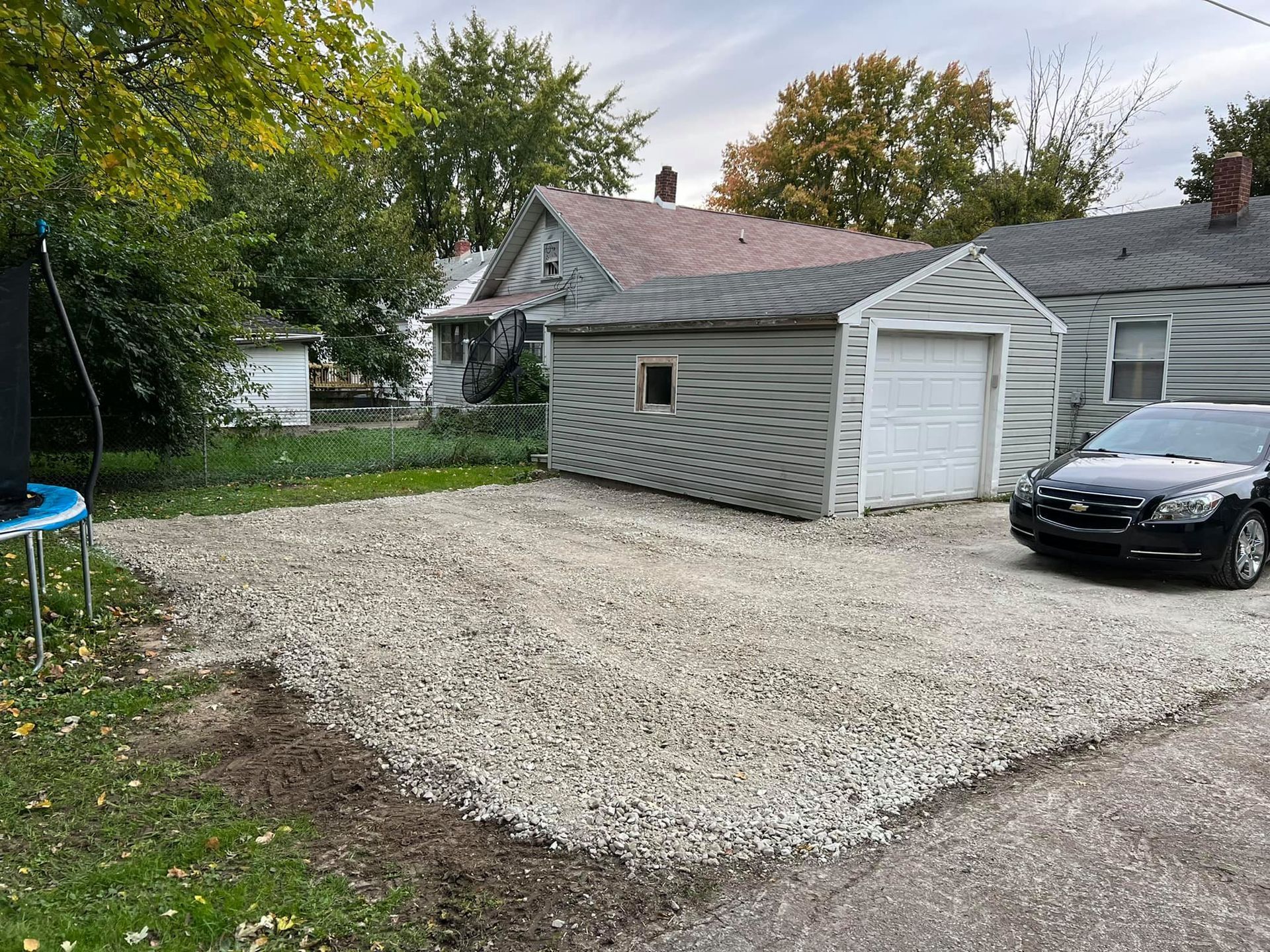 A car is parked in a gravel driveway in front of a house.
