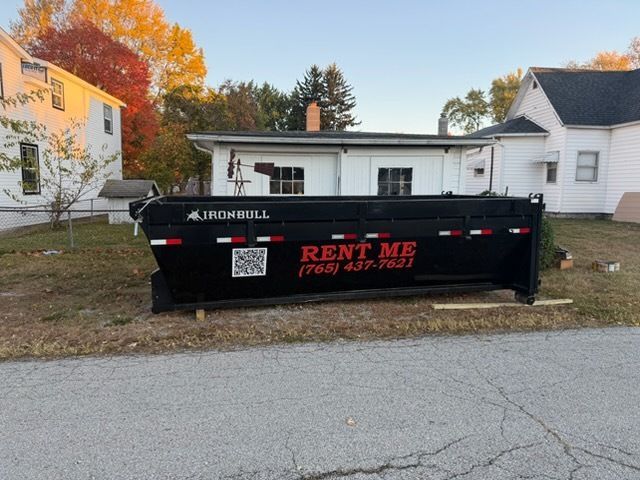 A black Iron Bull dumpster sits on a residential lawn, marked with 