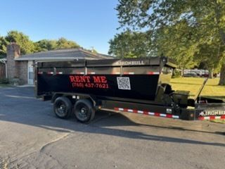 A black dump trailer parked on a driveway with 