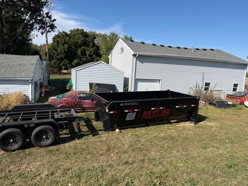 A dump trailer filled with wood is parked in a gravel lot.