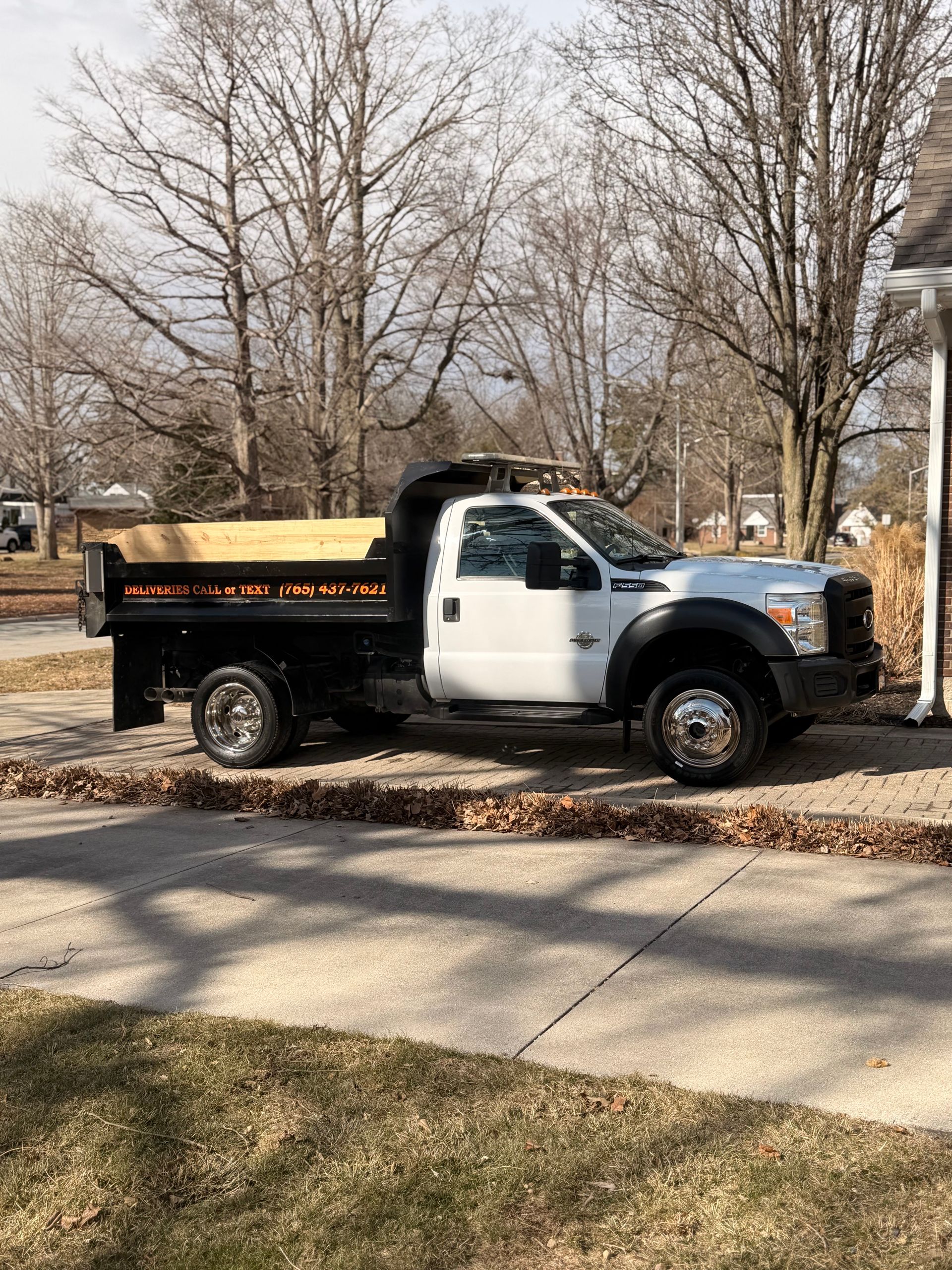 A white Ford dump truck with a black bed parked in a residential driveway on a sunny day.