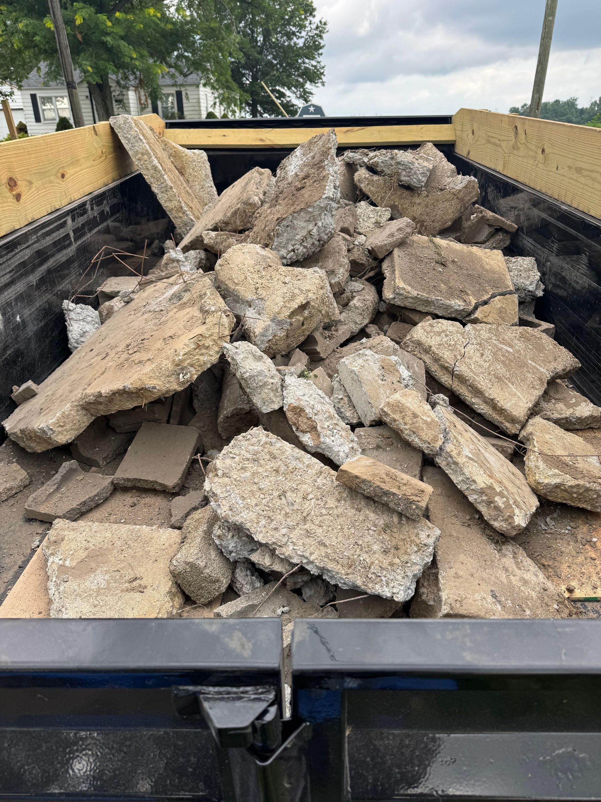 A truck bed filled with broken, jagged pieces of gray concrete slabs under a cloudy sky.