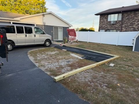 An outdoor area showing wooden framing boards placed on the ground, partially covered with black landscape fabric.