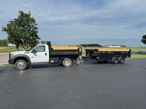 A white dump truck is parked on an asphalt lot, towing an empty black dump trailer with wooden side boards.