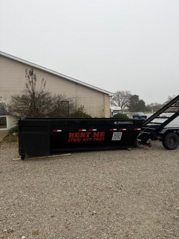 A black dump trailer parked on a gravel lot next to a building, with 