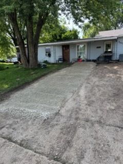 A light blue, single-story house with a partially paved gravel driveway leading to the front entrance.