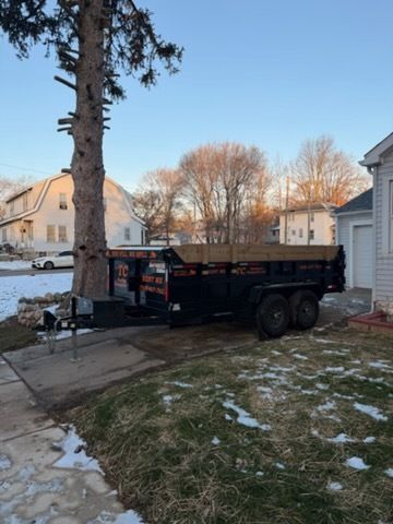 A black dumpster trailer parked on a residential driveway in a neighborhood with patches of snow.