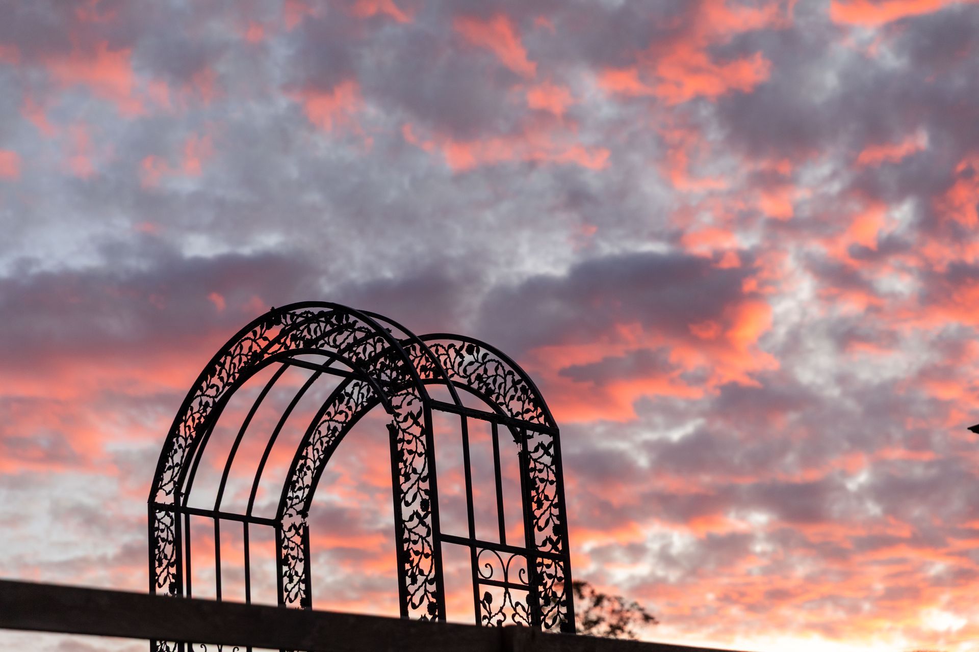 Black metal archway silhouetted against a vibrant sunset sky with pink and orange clouds.