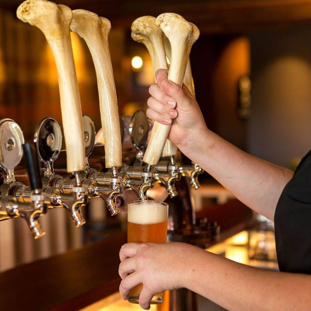 A bartender pouring beer from a tap with bone-shaped handles. The setting is a bar.