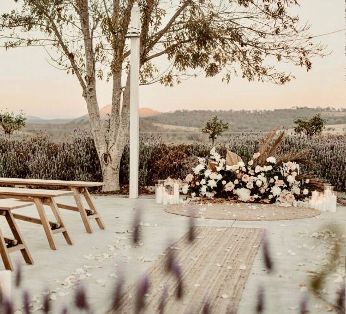 Wedding ceremony setup outdoors with white floral arrangement, lavender field, and scenic view.