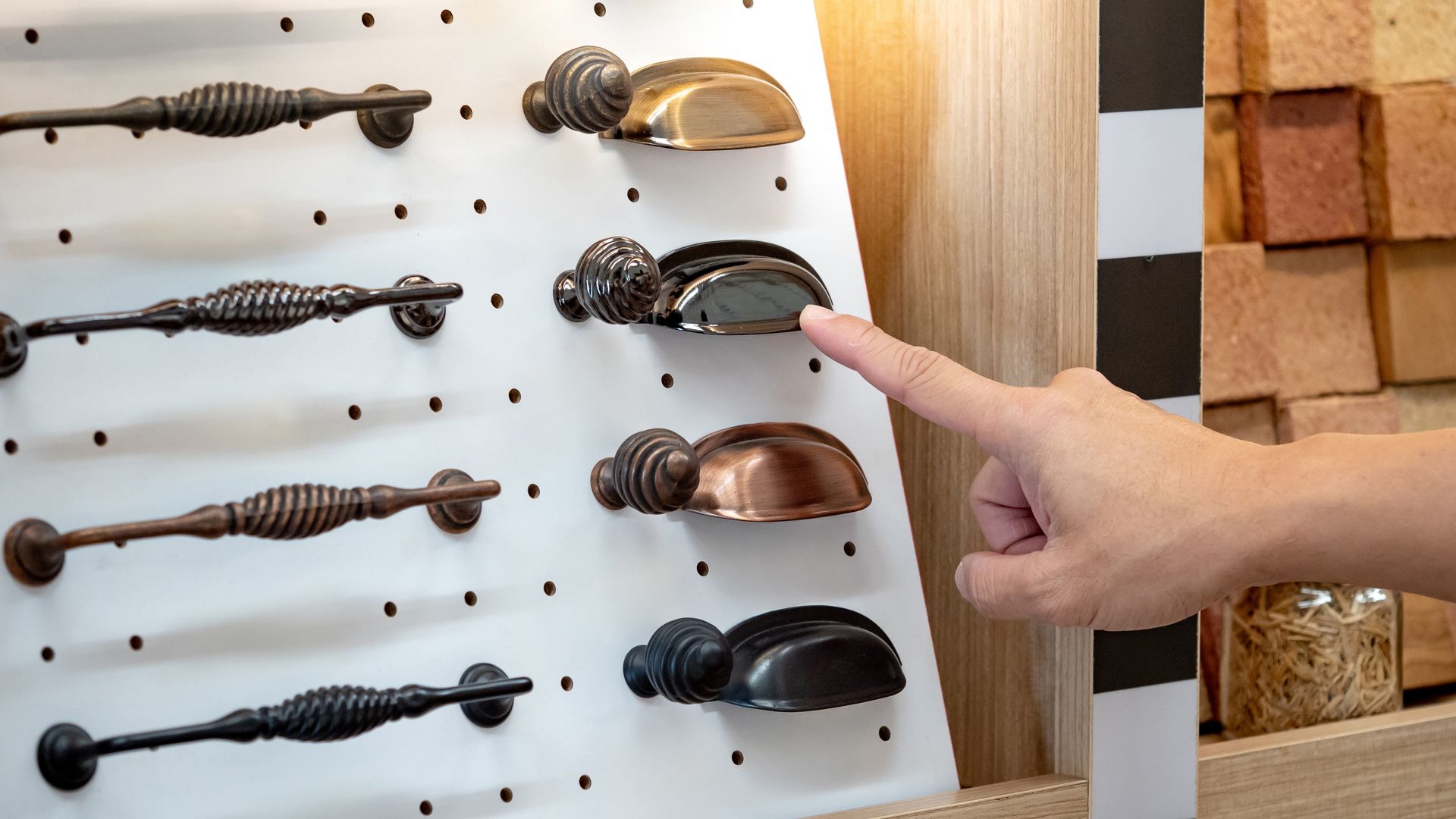 Hand selecting decorative cabinet hardware from a display board.