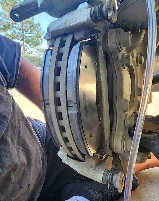 Person working on a car brake assembly. Brake pads are visible, as well as the caliper and rotor.