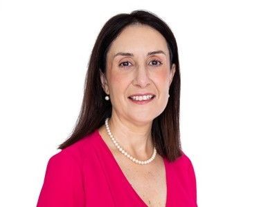Portrait of a smiling woman in a bright pink top and pearl necklace against a white background