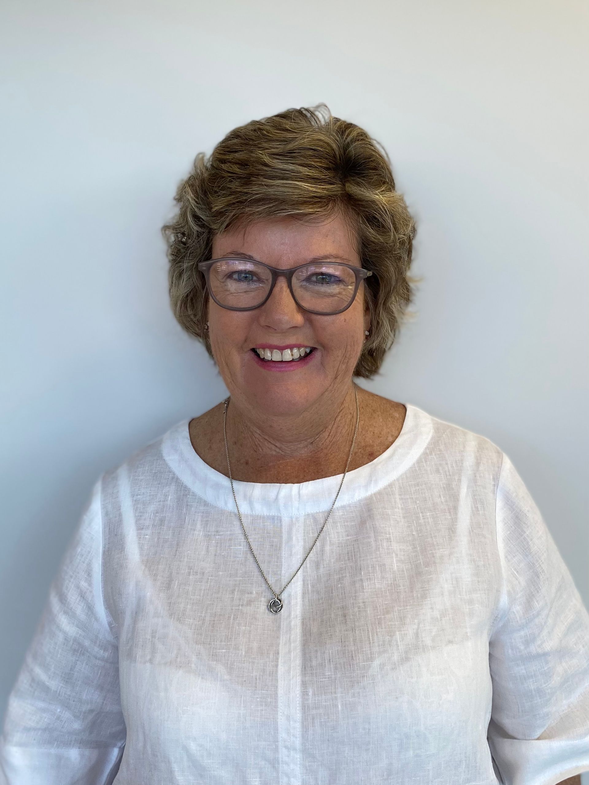 Smiling woman wearing glasses and a white blouse against a light background