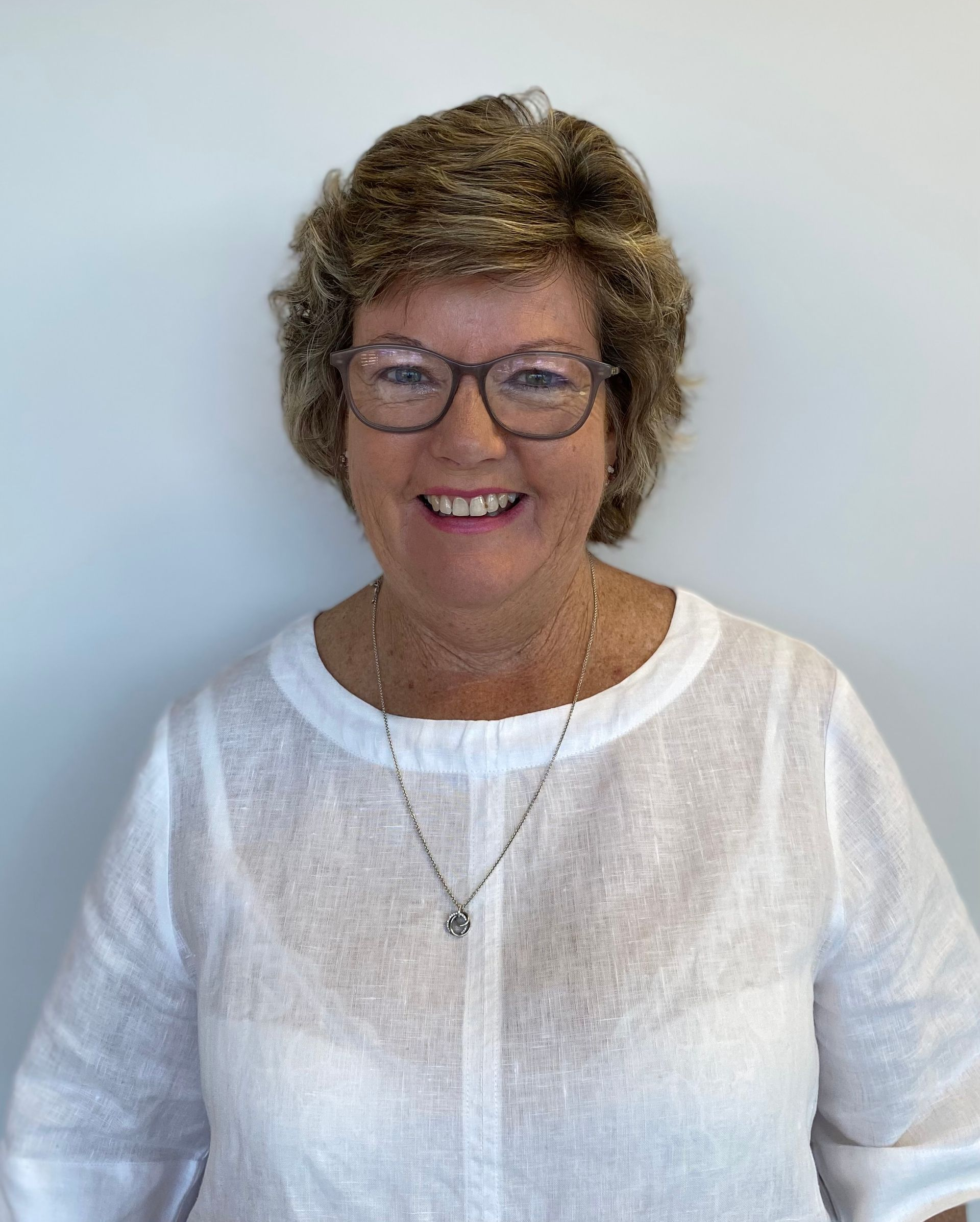 Smiling woman wearing glasses and a white top against a plain light background