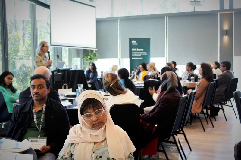 Audience seated at round tables in a conference room, listening to a speaker off-camera.