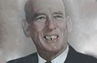 Portrait of a smiling man in a dark suit with missing front teeth against a light background