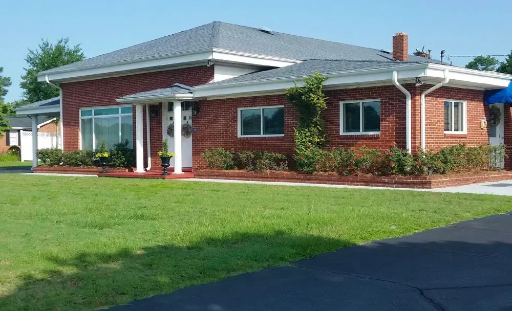 Red brick community building with white trim and a small covered entrance, set beside a grassy lawn.