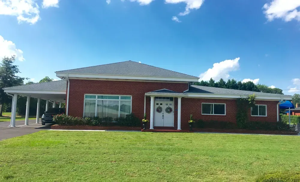 Single-story red brick house with white trim, front lawn, and carport under a bright blue sky