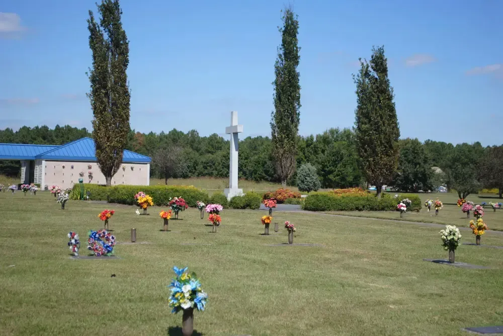 Graves decorated with colorful flower arrangements in a cemetery under a clear blue sky.