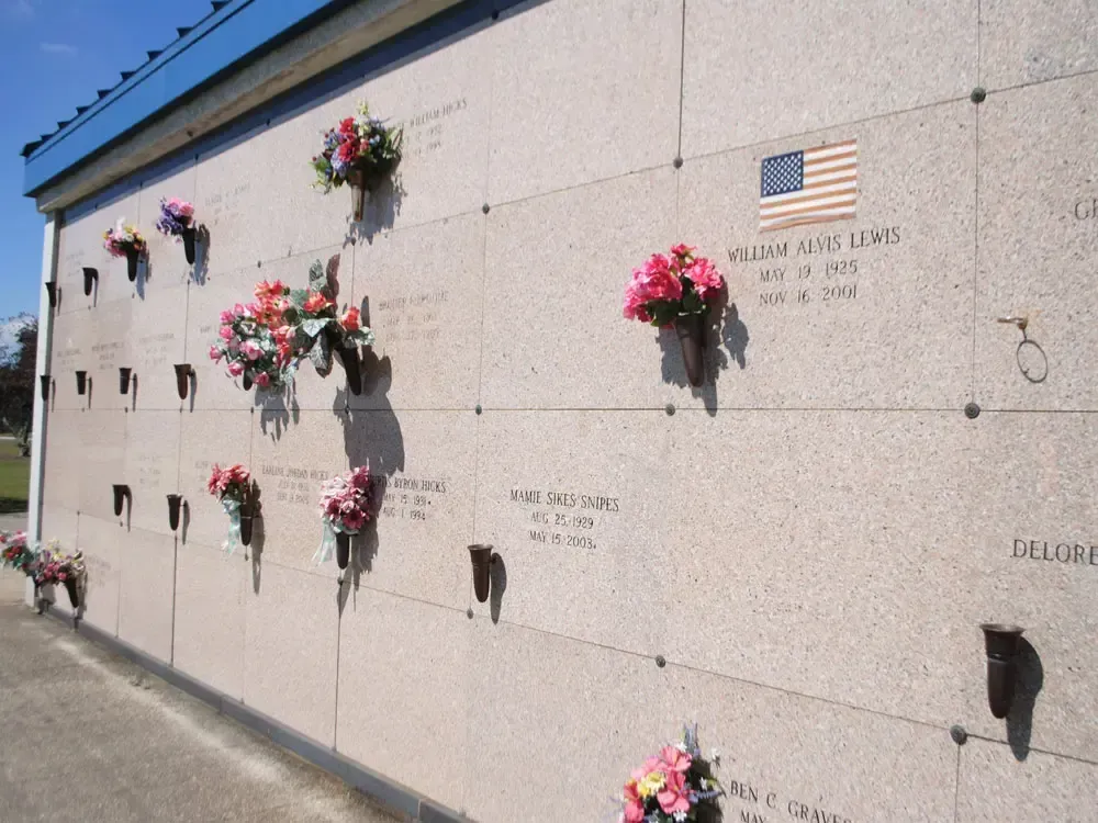 Wall of above-ground cemetery niches with flowers and plaques beside a walkway