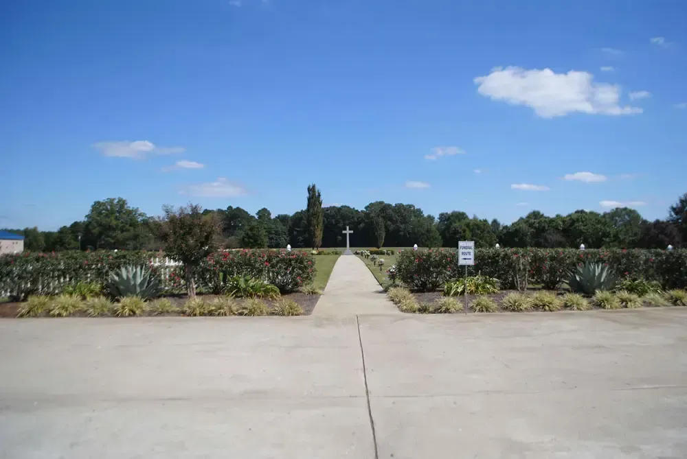 Memorial garden with a cross at the end of a paved path under a blue sky