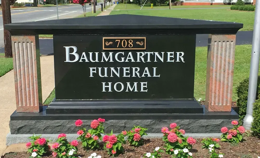 Baumgartner Funeral Home sign in a flower bed beside a sidewalk