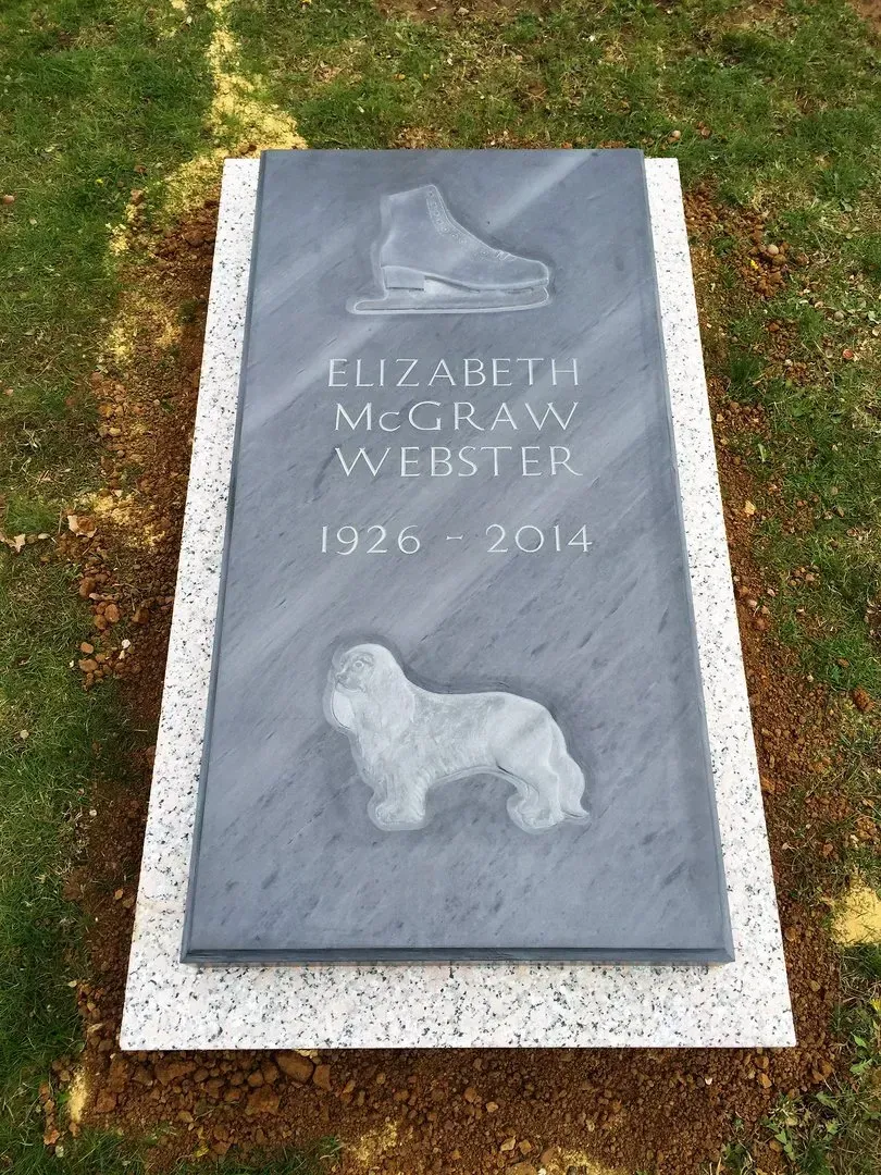 Gravestone for Elizabeth McGraw White with a carved dog, set in grass.