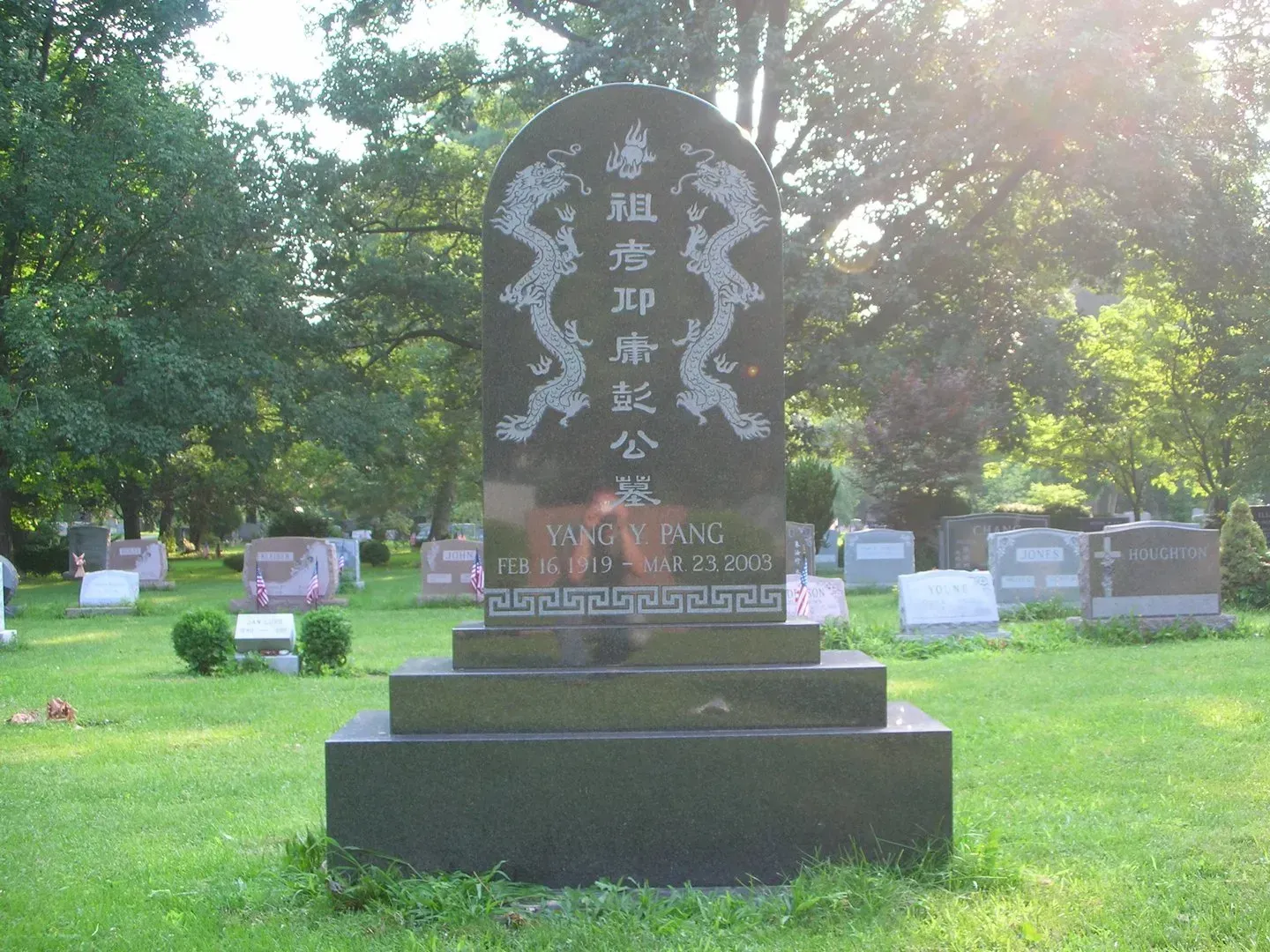 Stone memorial gravestone in a green cemetery with Chinese inscription, lit by sunlight.