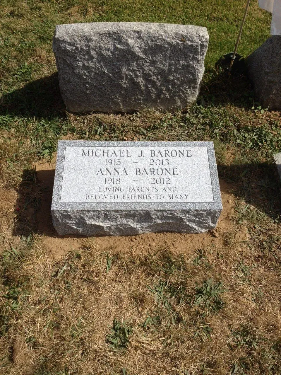Gravestone in a grassy cemetery with a smaller memorial marker in front.