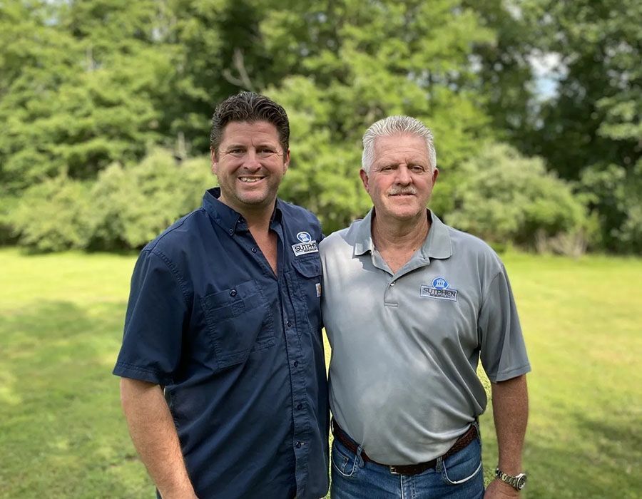 Two men standing together outdoors in a green park, smiling at the camera.