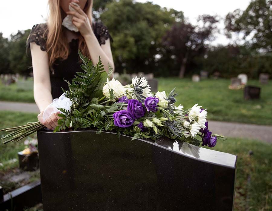 Woman placing purple and white flowers on a gravestone in a cemetery