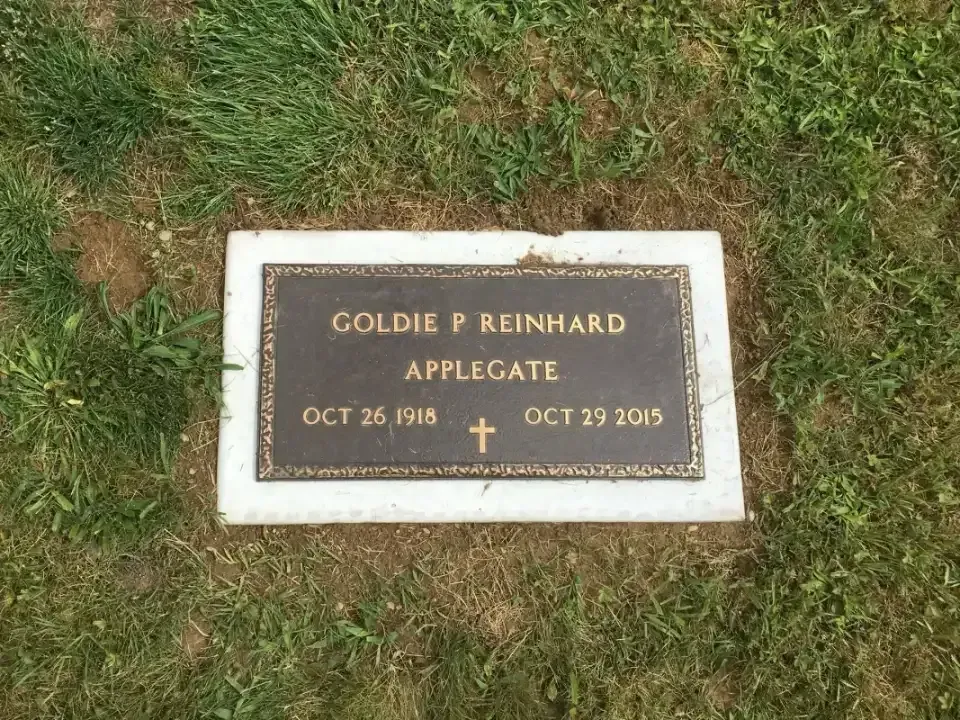 Gravestone plaque in grass with engraved name and dates, bordered in white marble.