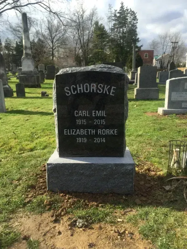 Black gravestone with the name Schorske in a cemetery, with trees and other headstones in the background