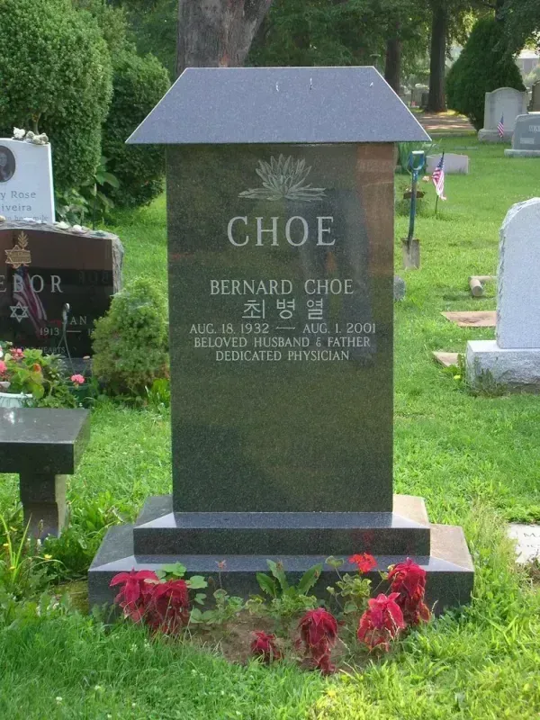 Black granite gravestone with flowers in a cemetery, engraved “CHOE.”