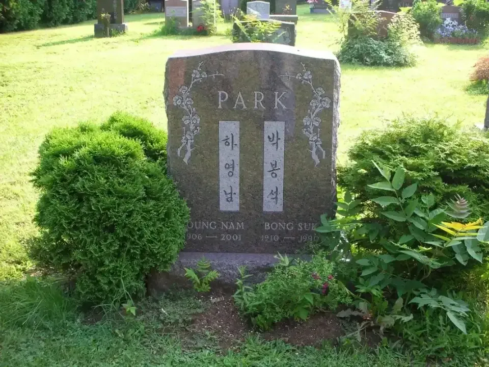 Stone park memorial surrounded by green shrubs and grass in a sunny garden.