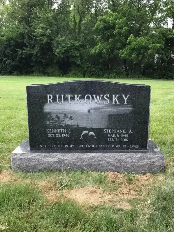 Black granite gravestone engraved “RUTKOWSKY” on a grassy lawn with trees behind it