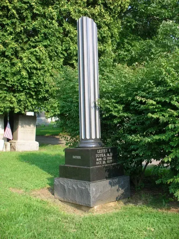 Tall silver striped monument on a black base in a grassy, tree-lined park