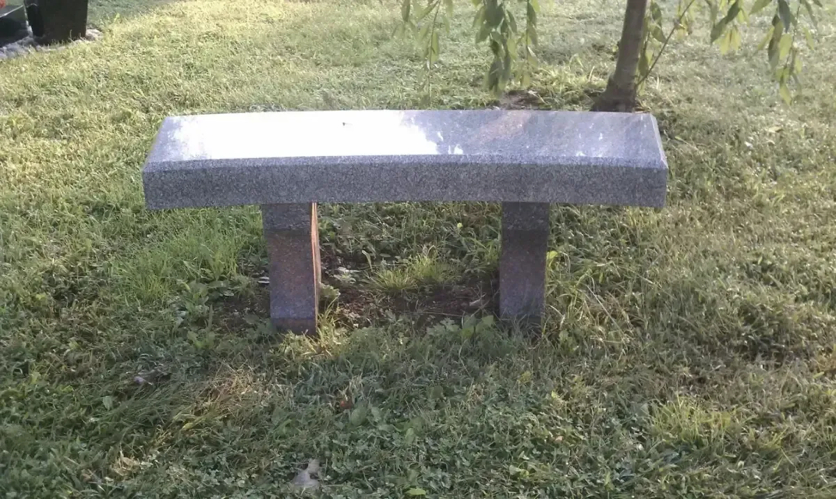 Gray stone bench on a grassy lawn with two brick supports