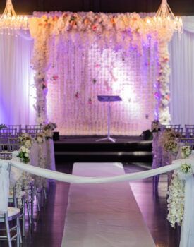 A wedding ceremony is taking place in a room decorated with flowers and chairs.