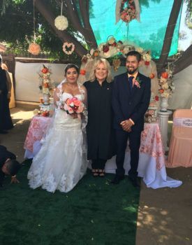 A bride and groom are posing for a picture with their wedding officiant.