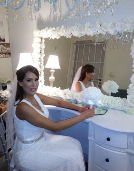 A bride in a white dress is sitting at a vanity in front of a mirror.