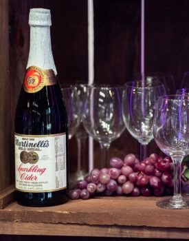 A bottle of sparkling cider next to a bunch of grapes and wine glasses