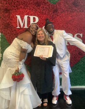 A bride and groom are posing for a picture with a woman holding a certificate.